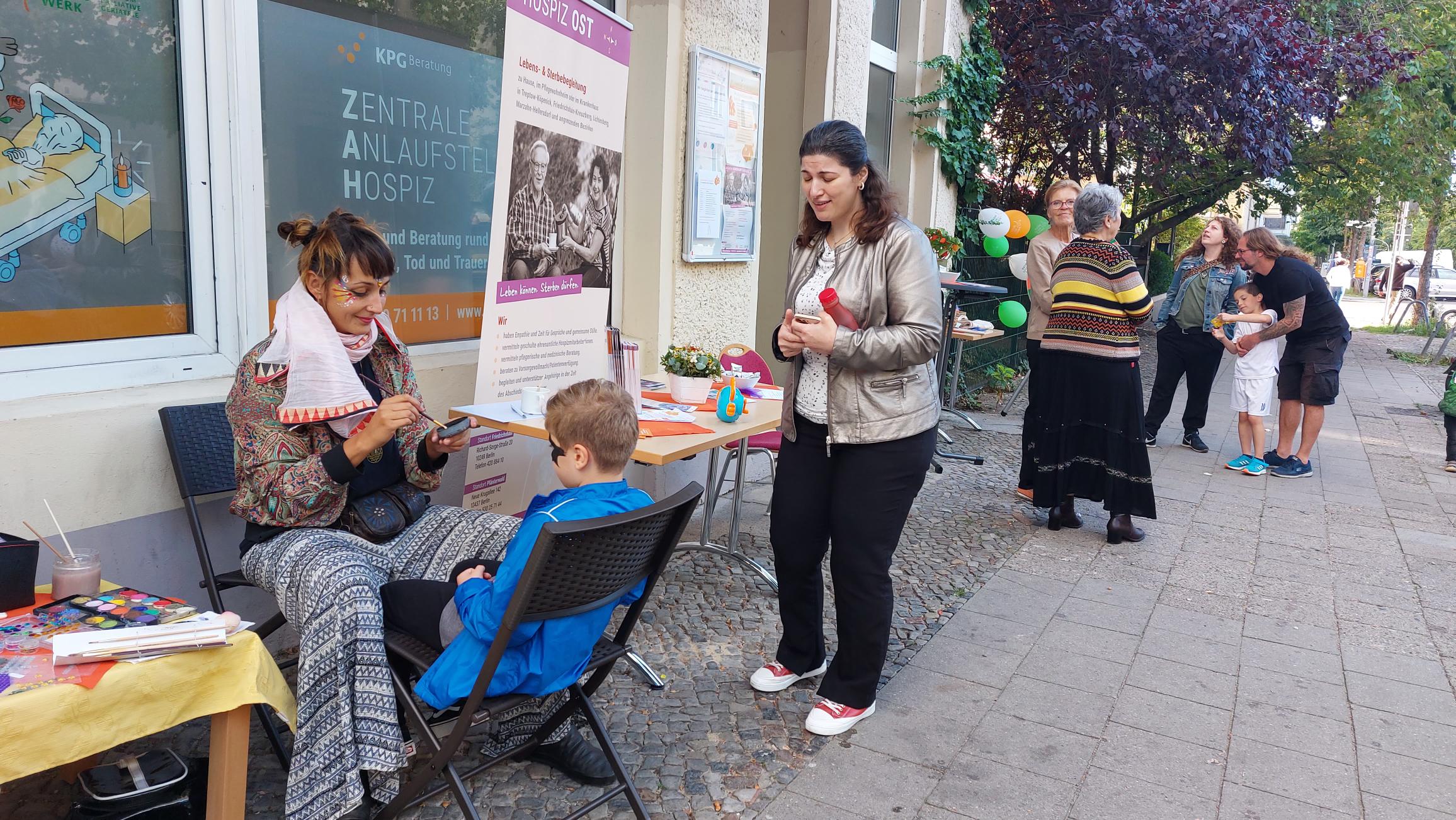 Kinder sitzen auf der Straße und werden geschminkt.